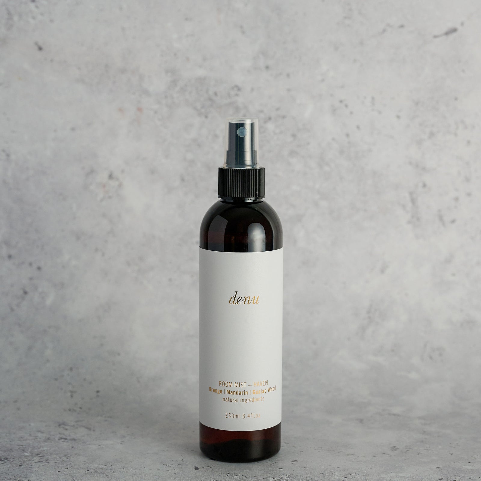 Hand holding a 'denu' Haven room mist bottle with an orange and plant in the background