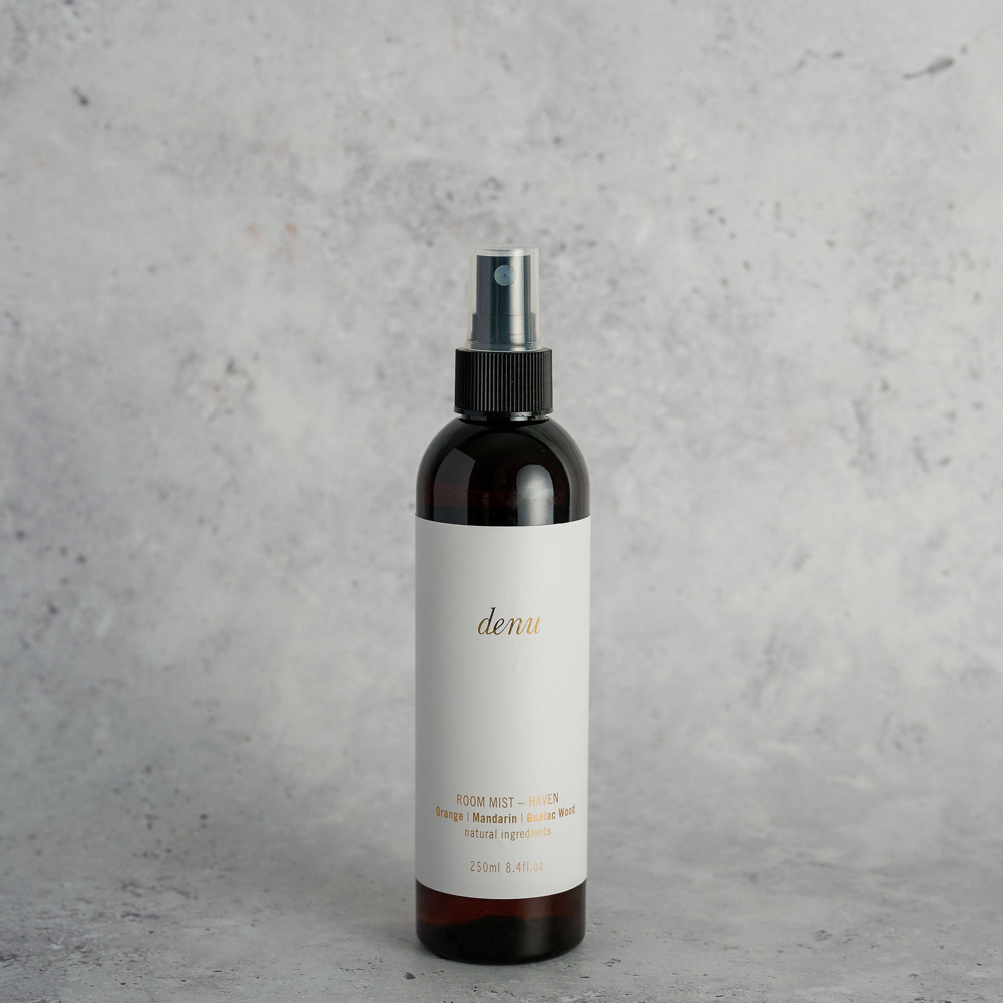 Hand holding a 'denu' Haven room mist bottle with an orange and plant in the background